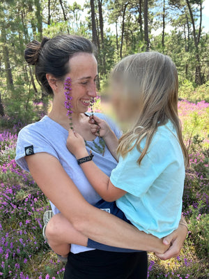 Unser Kind im Kids Shirt Isko in Caribbean Blue auf Lauras Arm in der blühenden Heide, Gesicht unkenntlich gemacht