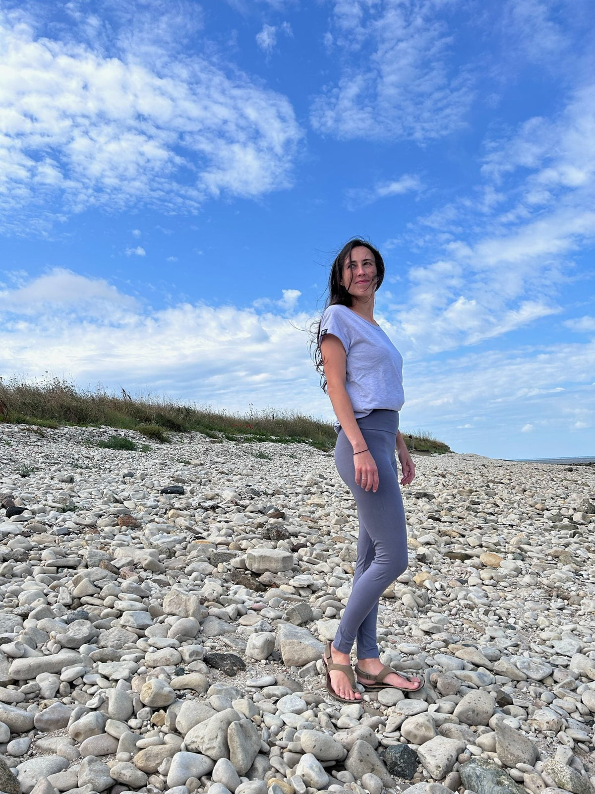 Laura trägt das Unisex T-Shirt Lasse in Lavender an einem Kiesstrand