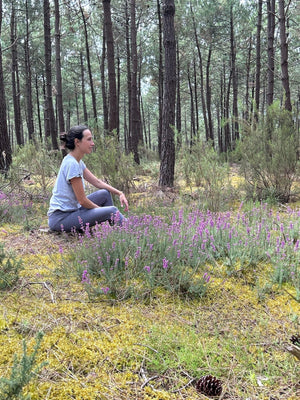 Laura im T-Shirt Lasse in Lavender sitzt im Kiefernwald zwischen blühender Heide